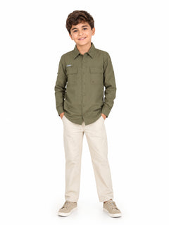 Niño vistiendo camisa de manga larga color verde militar y pantalones beige sobre fondo blanco.