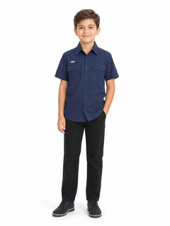 Niño vistiendo una camisa casual color navy de manga corta con bolsillos frontales y pantalones negros.