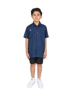 Niño vistiendo una camisa casual color navy de manga corta con bolsillos frontales y pantalones negros.