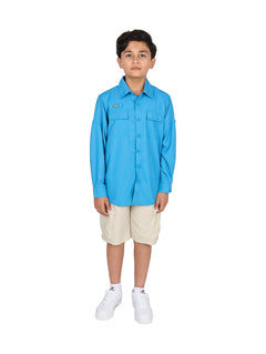 Niño modelando una camisa azul de manga larga, pantalones beige y tenis blancos sobre fondo blanco.